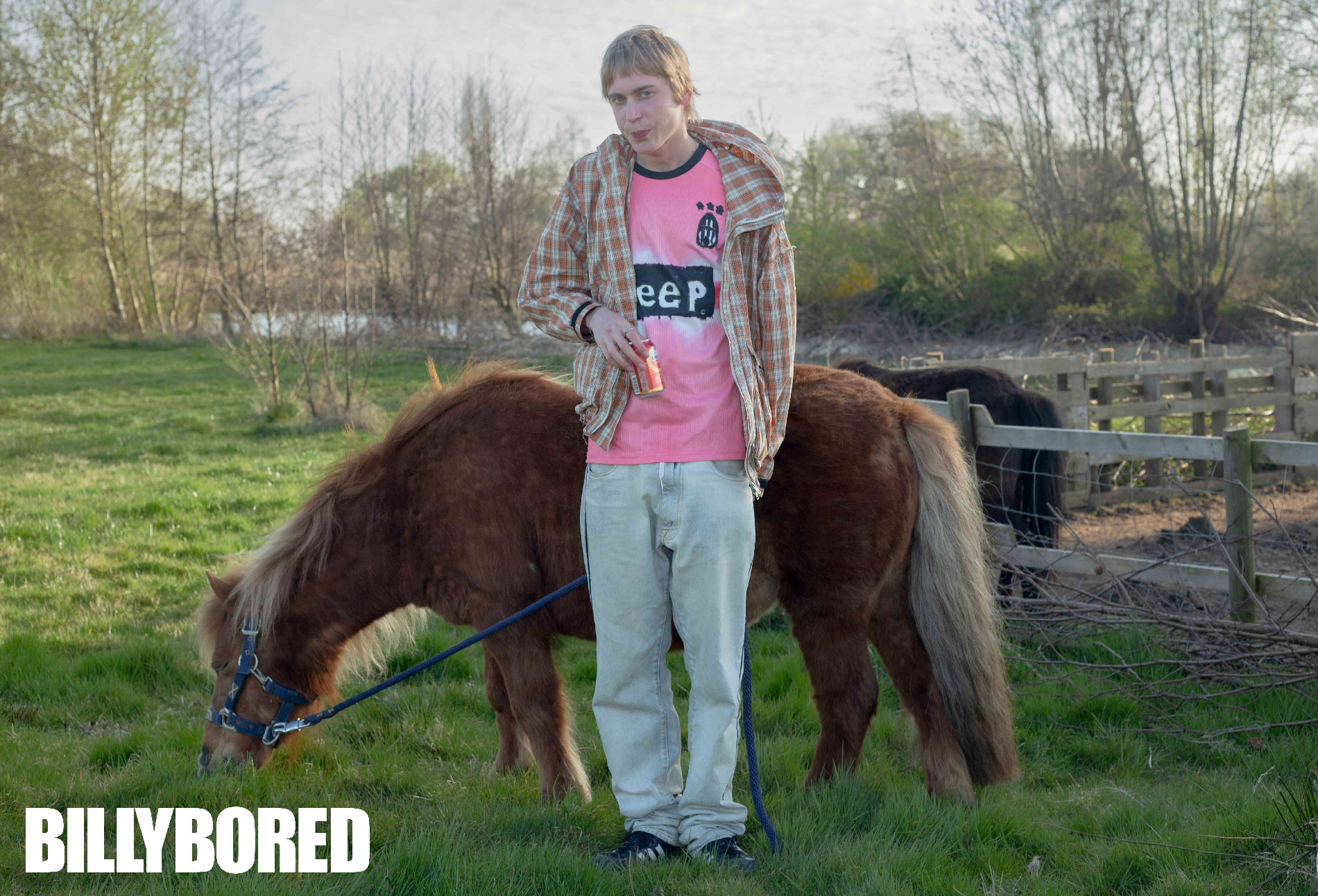 Young man in a pink shirt standing with a pony in a field, BILLYBORED fashion ad campaign