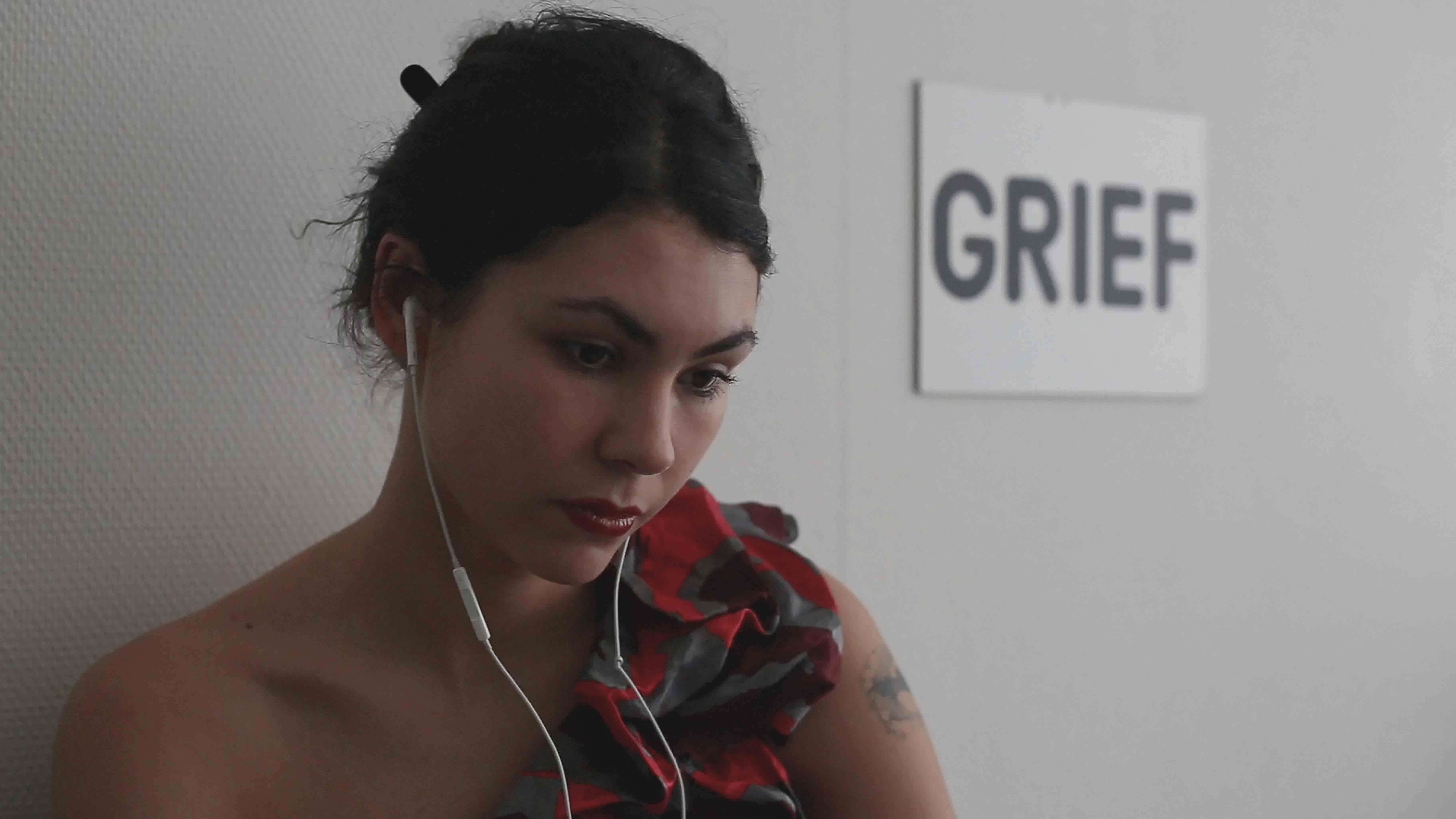 Woman in a red ruffled top in front of a "GRIEF" sign, Grant Me Virtue But Not Yet