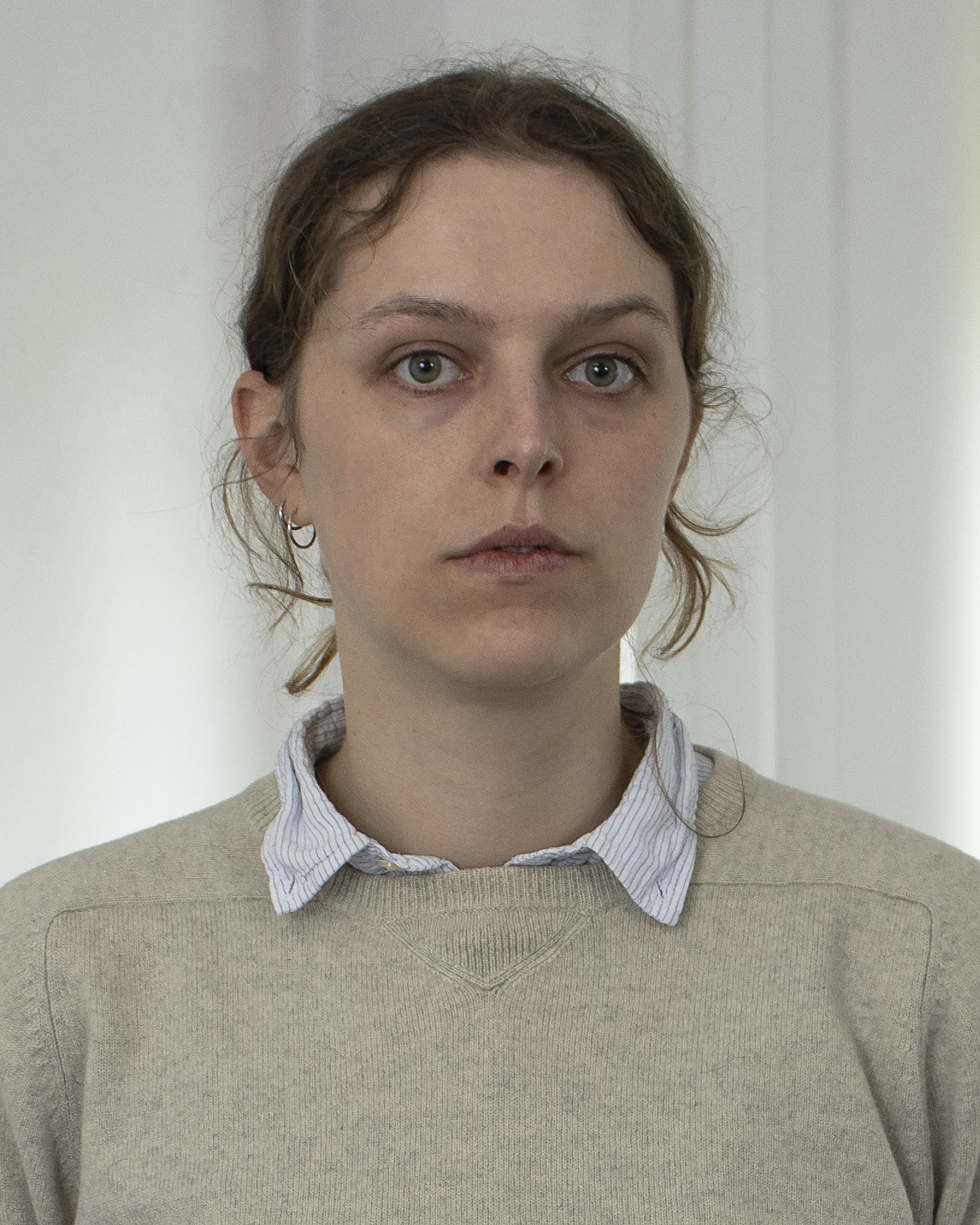 Portrait of a woman in a beige sweater and collared shirt against a white wall